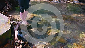 A beautiful girl wets her feet in a cold mountain river