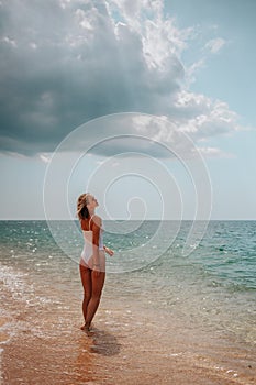 Beautiful girl in a white bodysuit walks along the shore of the azure sea