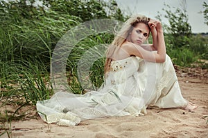 Beautiful girl in a white dress is sitting on the beach and looking back.