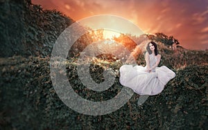 Beautiful girl in a white dress sitting in the garden at sunset.Fashion, wedding, fantasy concept.