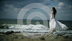 Beautiful girl in a white dress stands on seashore.