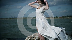 Beautiful girl in a white dress stands on seashore.