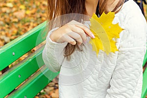 Beautiful girl in a white jacket and black pants with yellow leaves in the hands of sitting on the bench in autumn Park
