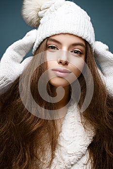 Beautiful girl in a white knitted hat with fur pompom. Model with gentle nude make-up. Cozy winter picture.