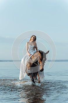 Beautiful girl in a white long dress riding a horse. Bride in the lake on horseback.