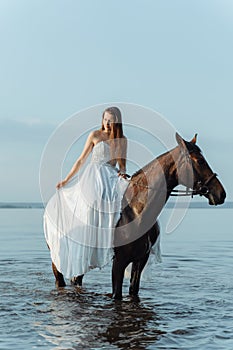 Beautiful girl in a white long dress riding a horse. Bride in the lake on horseback.