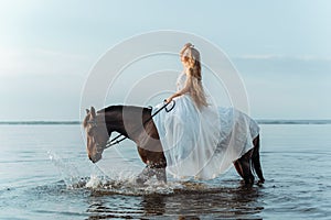 Beautiful girl in a white long dress riding a horse. Bride in the lake on horseback.