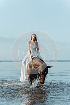 Beautiful girl in a white long dress riding a horse. Bride in the lake on horseback.