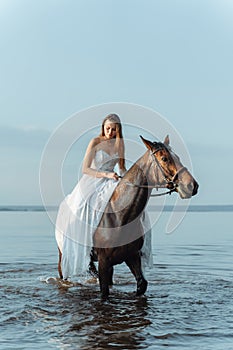 Beautiful girl in a white long dress riding a horse. Bride in the lake on horseback.