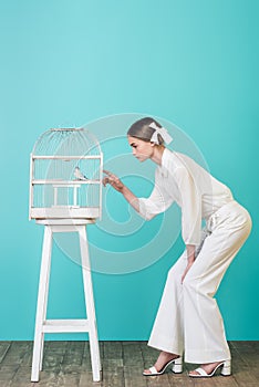 beautiful girl in white outfit looking parrot in cage