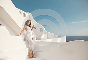 Beautiful girl in white outfit. Model on summer vacation enjoying time on Santorini island Greece. Brunette posing on white