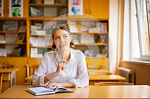 Beautiful girl in a white shirt sitting at the table by the window in the classroom reading a book