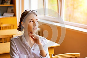 Beautiful girl in a white shirt sitting at the table by the window in the classroom reading a book