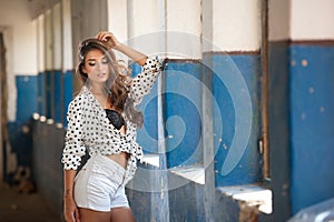 Beautiful girl with white shirt and white shorts posing in old hall with columns blue painted.