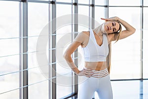Beautiful girl in white sportswear warms up against the background of panoramic windows.