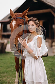 Beautiful girl in a white sundress next to a horse on an old ranch