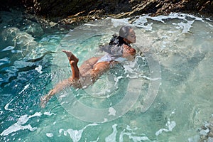 Beautiful girl in a white swimsuit swims in a natural stone pool