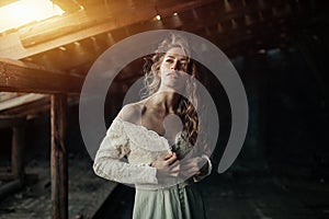 Beautiful girl in in white vintage dress with curly hair posing on the attic. Woman in retro dress. Worried sensual emotion . Retr