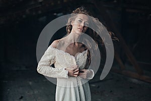 Beautiful girl in in white vintage dress with curly hair posing on the attic. Woman in retro dress. Worried sensual emotion . Retr