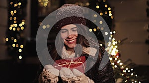 Beautiful girl in winter clothes hugging red present box looking happy and smiling looking to camera. She standing at