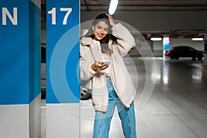 Beautiful girl in wireless earphones and mobile phone in hands in the underground parking.