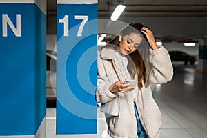 Beautiful girl in wireless earphones and mobile phone in hands in the underground parking. Portrait of modern young woman with sma