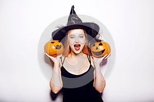 Beautiful girl witch is holding a pumpkin in her hands. Woman celebrating halloween, joy and a smile on her face
