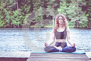 Beautiful girl in a yoga pose on the lake. Lotus position , Padmasana. The concept of appeasement,  healthy lifestyle. Space for