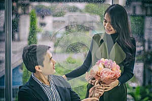 Beautiful girlfriend offers bouquet of roses to young businessman sitting, To congratulate successful business