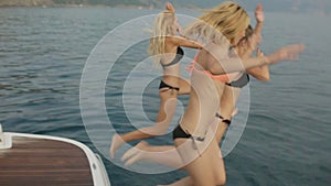 Beautiful girls in bikinis having fun and jumping from the yacht into the sea