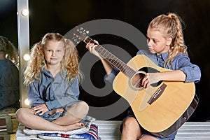Beautiful girls blonde sisters in a cozy environment learn to play the guitar.