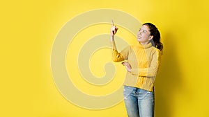 Beautiful girls smiling happy pointing upwards in studio yellow background