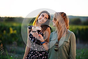 Beautiful girls tasting wine in a field near vineyard field. Celebrating successful harvest season. Couple having a romantic date