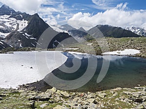 Beautiful glacial lake with springs from melting ice glacier with sharp snow-capped mountain peaks reflecting on water