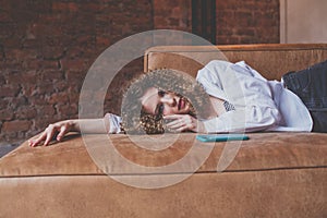 Beautiful glamorous woman in white shirt with curly hair resting on the sofa with green mobile phone near