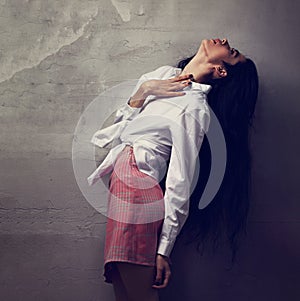Beautiful glamour female model with long black hair posing in white shirt and red skirt on grey studio wall background