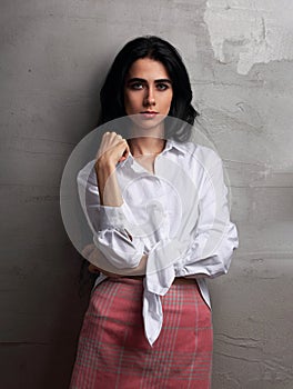 Beautiful glamour female model with long black hair standing and thinking in white shirt and red skirt on grey studio wall