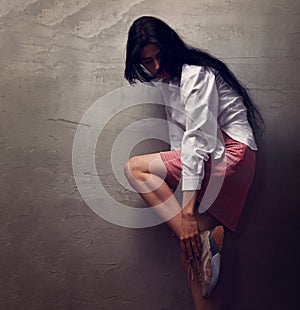 Beautiful glamour female model with long black hair wearing fashion sneakers shoes in white shirt and red skirt on grey studio