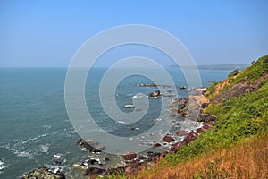 Beautiful Goa beach, rocky coast and blue sea view from high green cliff, India at the clear sky background