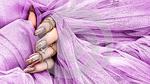 Beautiful gold manicure nails on pink tulle background . Manicure and nails concept. Trendy nails