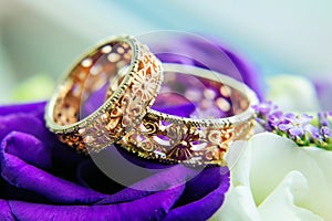 Beautiful gold wedding rings with patterns, close-up. Two gold rings, blurred background with white and blue flowers