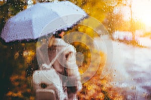 Beautiful golden autumn season. Watercolor like blurred blond girl with backpack and bright umbrella stands under rainy