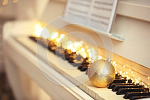 Beautiful golden bauble and fairy lights on piano keys, space for text. Christmas music