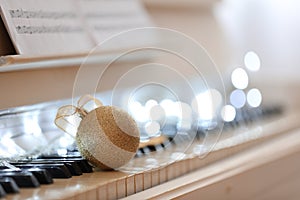 Beautiful golden bauble and fairy lights on piano keys, space for text. Christmas music