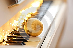 Beautiful golden bauble and fairy lights on piano keys, space for text. Christmas music