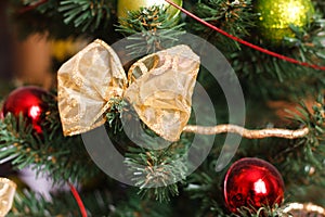 Beautiful golden bow and red, green Christmas balls on artificial Christmas tree close up detail