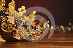 Beautiful golden crown and fairy lights on wooden table, closeup. Fantasy item