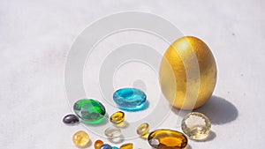 Beautiful golden egg and colorful jewels on white table in daylight