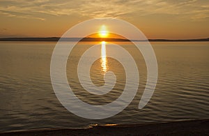 Beautiful golden orange sunset over the lake. The sun sets turning the sky yellow, orange & red tones & reflects in the lake