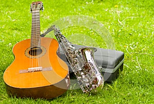 Beautiful golden saxophone and acoustic guitar lying across black instumental case on grassy surface